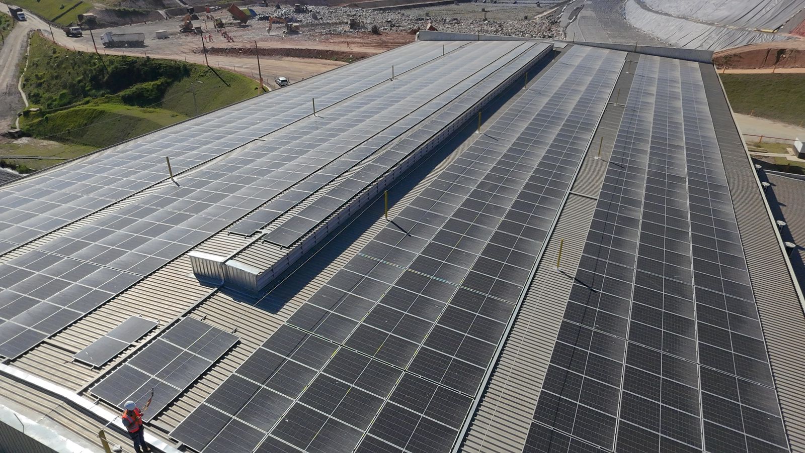 Cobertura industrial com usina solar de grande porte e técnico realizando manutenção, vista aérea